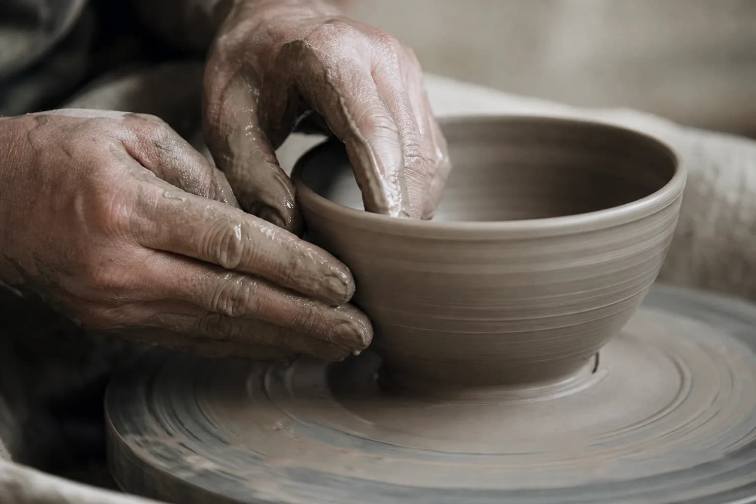 A potter's clay-slicked hands shaping the wall of a bowl on a spinning wheel.